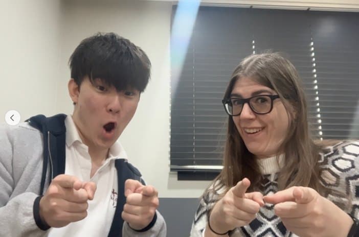A student and a teacher pointing at the camera in a classroom