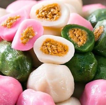 Pink, white and green songpyeon rice cakes, some broken open to show a sweet sesame filling