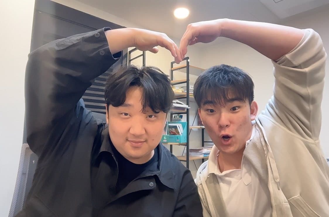 Two students making a heart shape over Mr. Chu for the camera