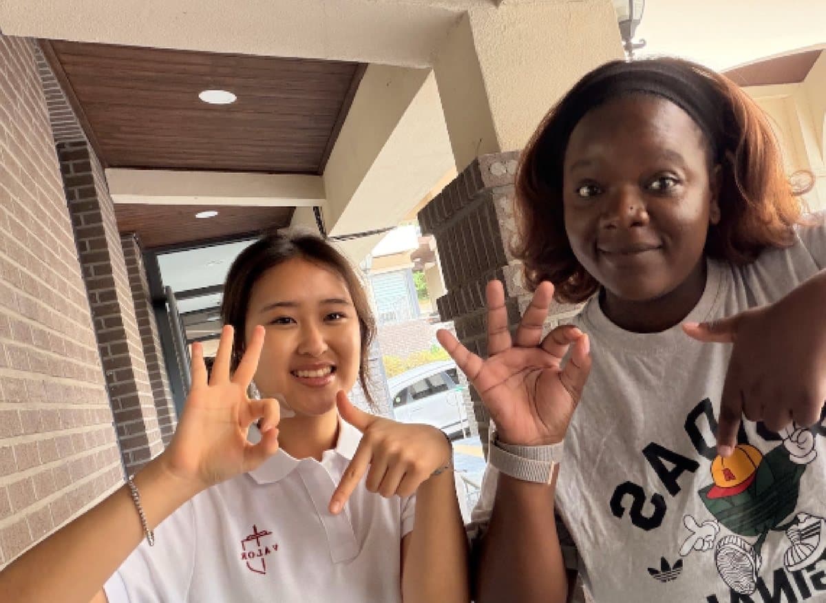 Mrs. Sibanda and a student making hand signs at the camera outside the school